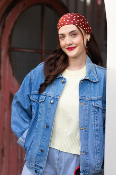 Adult female posing and leaning in arched door entry, wearing denim jacket red polka-dot headscarf