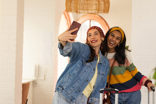 Two female friends posing and laughing while taking selfie in bright lobby with smartphone