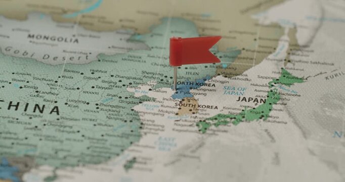 Close-up view of a person's hand placing a small red flag pin on the country of North Korea, marking it as a travel destination, a place of interest, or indicating a political situation