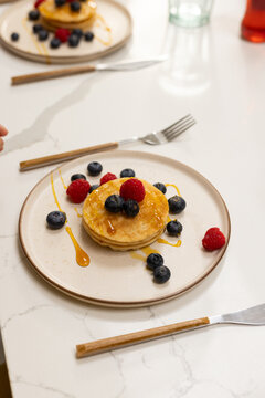 Pancake stack is sitting on beige plate on marble tabletop, syrup and blueberries glistening