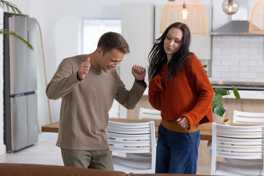 Couple dancing in home kitchen wearing beige and rust-orange sweaters by wooden table