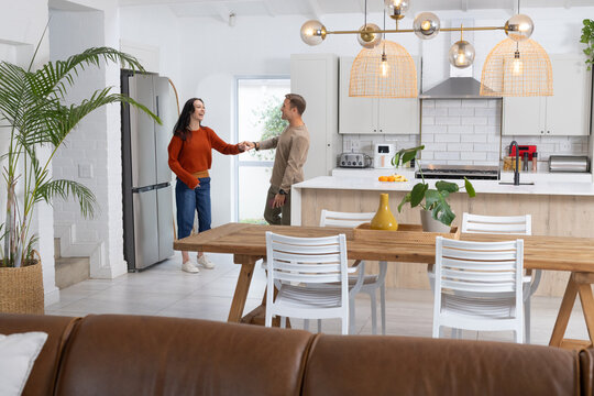 Couple handing keys while standing in kitchen near island with red coffee maker and wood table