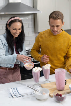 Couple making pink shakes in kitchen in denim jacket and mustard sweater with blender sprinkles