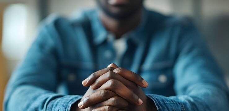 Close-up of a person with dark skin holding hands clasped together in a thoughtful gesture