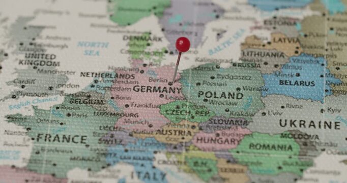 Close-up view of a person's hand placing a red pushpin on Berlin, Germany, on a map of Europe, marking the destination for a future travel plan or indicating a specific location of interest