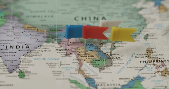 Colorful flag pushpins marking Thailand, Cambodia, Laos, and Vietnam on a political world map, with a shallow depth of field focusing on Southeast Asia, suggesting travel planning or destinations