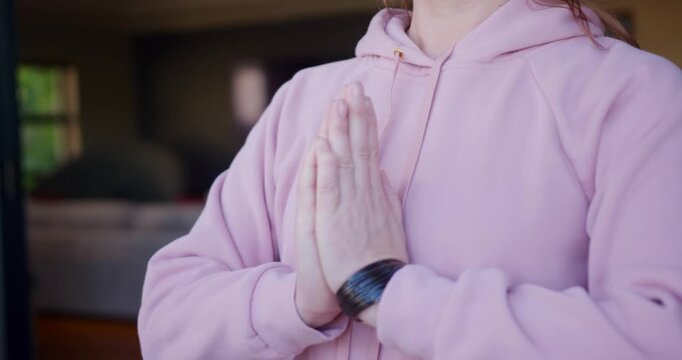 Mature woman inhaling, centering, placing palms, lowering hands and resting in pink hoodie at home
