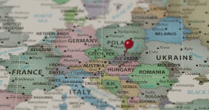 Close-up of a hand placing a red pushpin on the country of Slovakia on a political map of Europe, marking a specific travel destination, location, or strategic point of interest