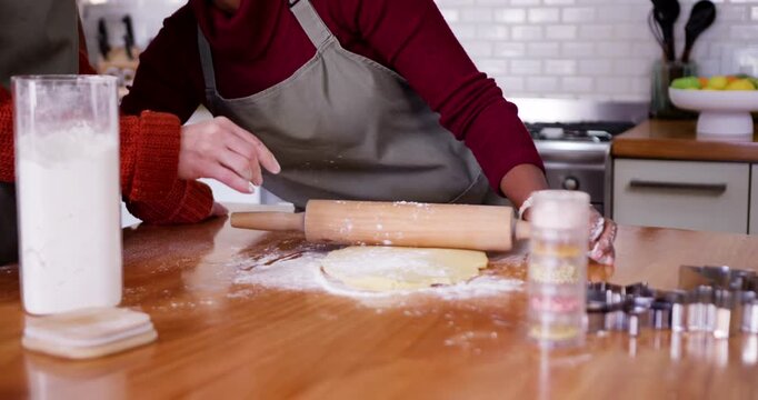 Two women rolling dough at counter after left woman sprinkling flour, aproned using pin for baking