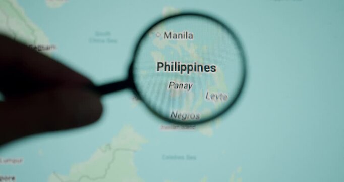 Close-up shot of a hand holding a magnifying glass over a digital map of the Philippines, focusing on the country and its capital, Manila, while planning a trip and researching a destination