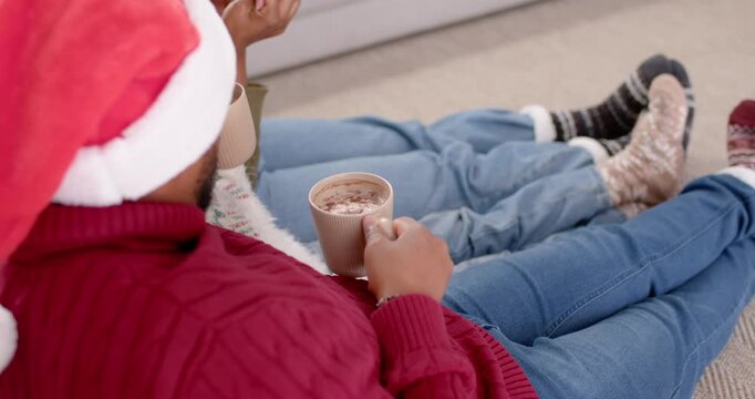 African American family holding mugs after hat cue, shifting from cocoa to festive socks on rug