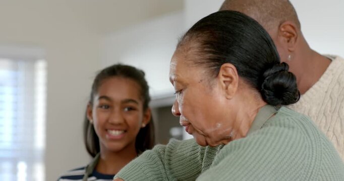 African American grandma seeing measuring cup, mixing in bowl in kitchen and guiding granddaughter
