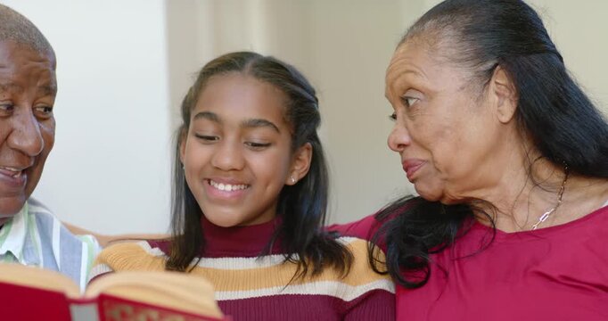 African American family encouraging teen grandkid reading after grandpa opening red book on couch