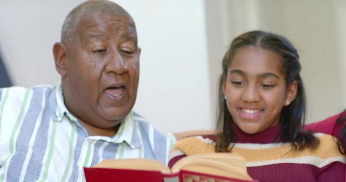 African American family reading red book on sofa, grandfather opening pages, sharing story