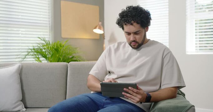 African American man after notification, tapping tablet in folio on sofa, reacting to funny content