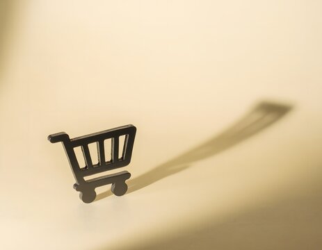 Small Black Shopping Cart Casting Large Dramatic Shadow on Cream Background, Minimal Ecommerce and Retail Concept
