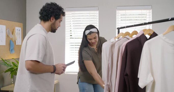 African American team in workroom when woman picking white tee inspecting rack and tablet to choose