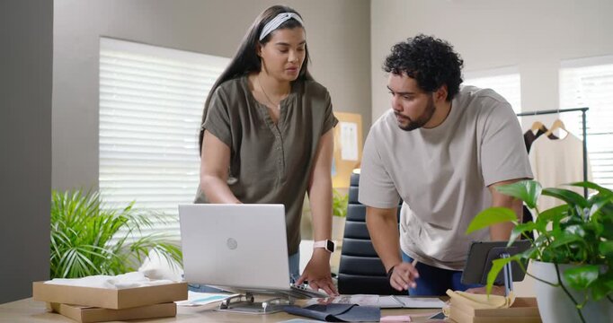 African American colleagues leaning over laptop and swatches, pointing and jotting for packaging