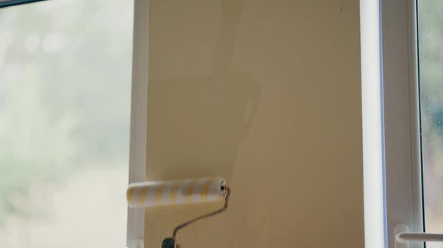 Paint roller applying primer or clear coat on wall near window, home renovation concept
