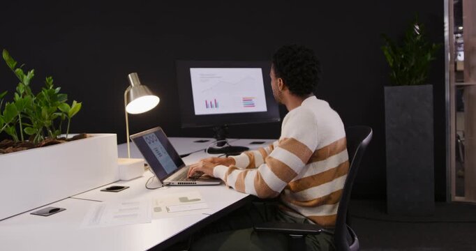 African American man typing, studying monitor charts and writing notes at office desk, copy space