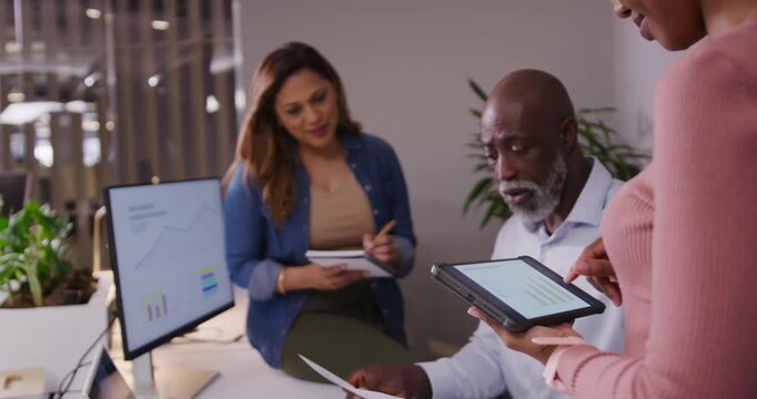 Diverse coworkers following presenter tapping tablet reading report comparing charts for review
