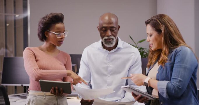 Diverse team aligning on pages after reading page pointing at tablet jotting in notepad in office