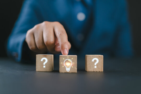 Creative idea and problem solving concept with hand holding lightbulb among question marks, symbolize innovation, solution finding, critical thinking and choosing the best answer in business strategy