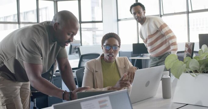 Team leaning in as left coworker showing tablet while woman typing at desk reviewing laptop charts
