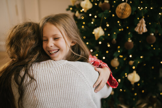 Happy mother and her 7-years old daughter hugging near decorated Christmas tree