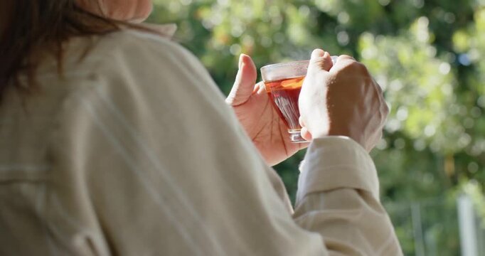 Camera panning is revealing hands cradling tea cup and are lifting toward mouth, sipping on balcony