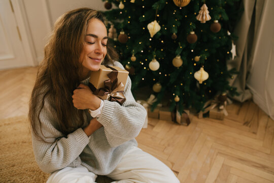 Young beautiful woman relaxing sitting under decorated Christmas tree.