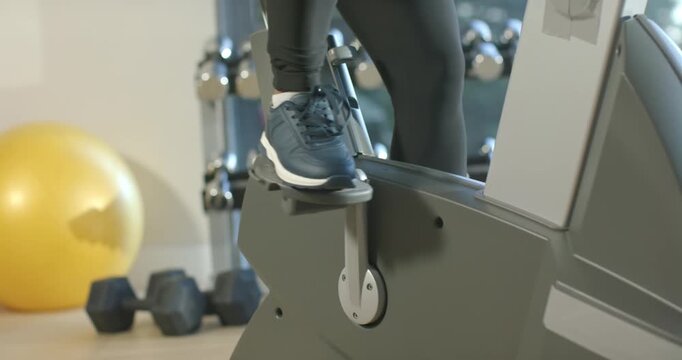 Pressing down with foot, legs are stepping on stepper with hex dumbbells in gym for cardio