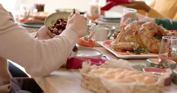 As diners are reaching across table, seated adult is scooping salad to serve family-style plates