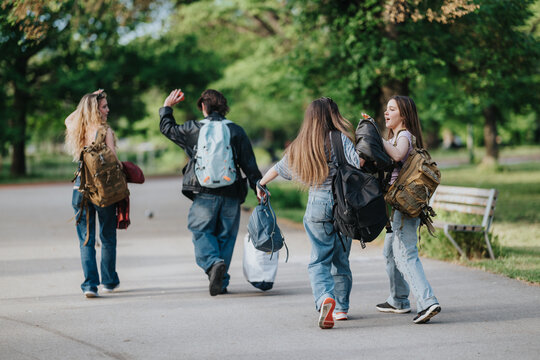 A group of teen friends walking together carrying backpacks along a tree-lined park path. Four teenagers chat and laugh while strolling through green outdoor surroundings.