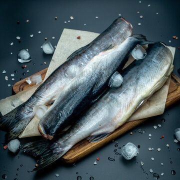 Raw pink salmon carcass on wooden board with ice cubes and spices top view