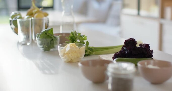 Camera is pulling back and shifting focus to reveal countertop ingredients and sunlit window view