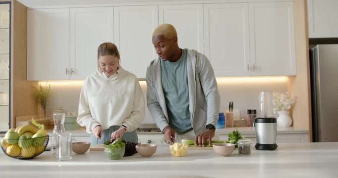 Diverse couple chopping greens and slicing celery on cutting boards at kitchen island starting meal