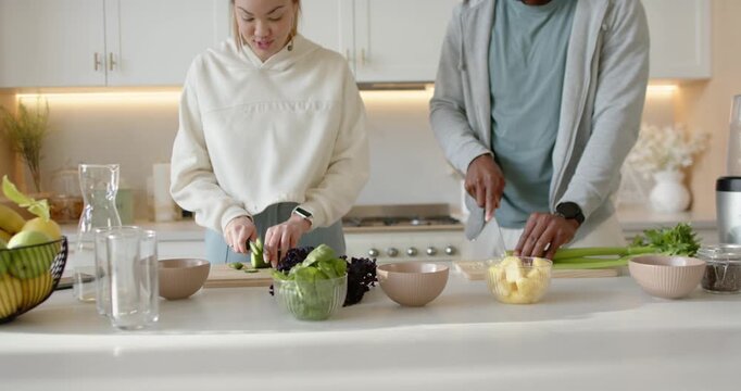 Couple chopping cucumbers and slicing pineapple at counter using cutting boards and bowls for salad
