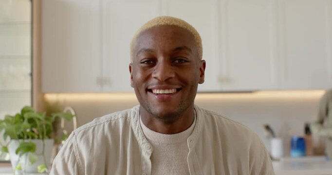 Camera framing African American man smiling, writing notes on laptop in kitchen during online call