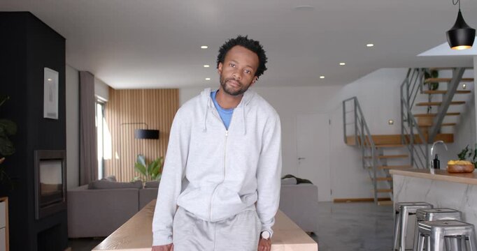 African American man facing camera cue at home, leaning on table, folding arms in gray hoodie