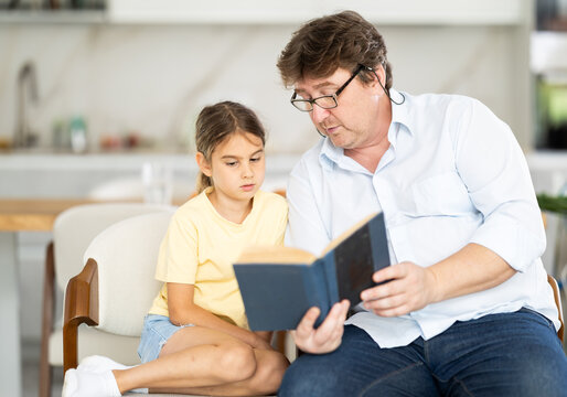 Father reads book to little cute daughter, spend leisure enjoy good life hobby and pastime at home. Fatherhood, upbringing, children development