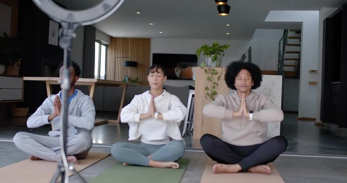 Diverse friends in hoodies on mats toward ringlight phone mount, shifting palms to knees, filming