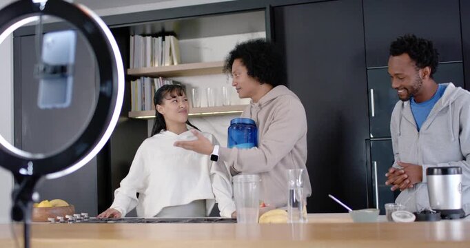 Diverse hosts demoing blue product to phone as ring light recording at kitchen island