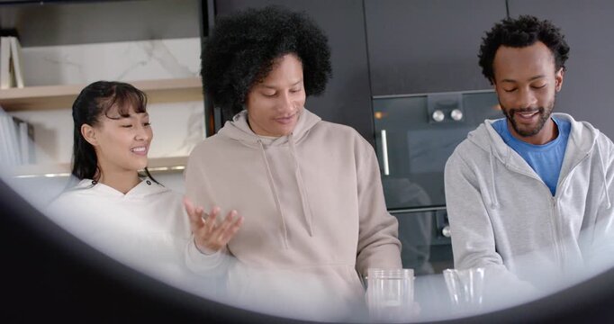 Diverse friends watching African American man telling joke, moving glasses at kitchen counter, ring