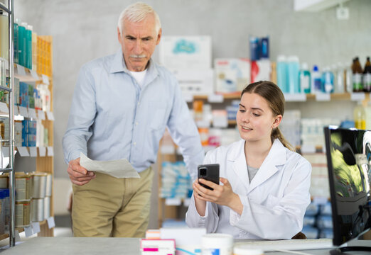 Young female pharmacist showing something on phone to male client in drugstore