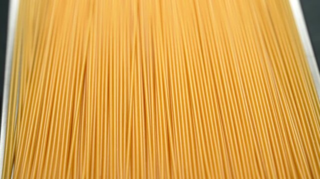 Close-up rotating view of uncooked raw spaghetti noodles.