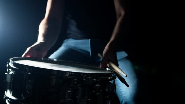 Drummer plays drum rudments, practise rolls, on snare drum. Dark background, high contrast. Slow motion. medium shot, dramatic backlight. 