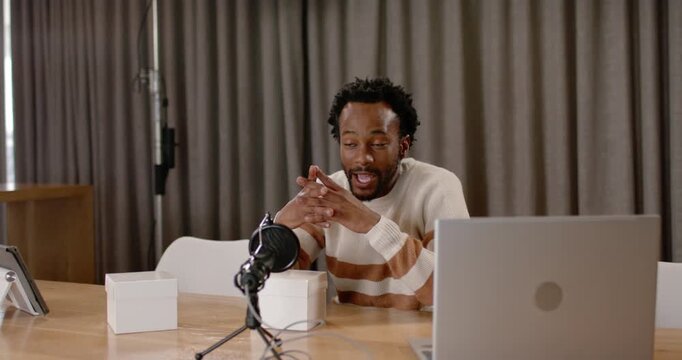 Recording man wearing jumper at studio speaking to mic checking laptop pointing at white boxes
