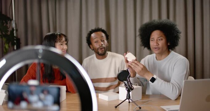 Diverse co-hosts filming on smartphone in ring light, unboxing round device and showing features