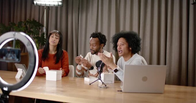 Co-hosts unboxing earbuds after camera prompt, inspecting charging case, testing fit for review